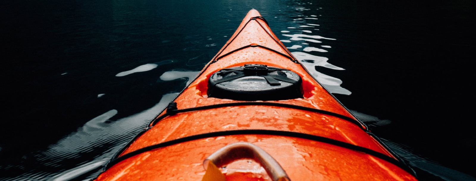 The bow of a kayak cutting through dark water